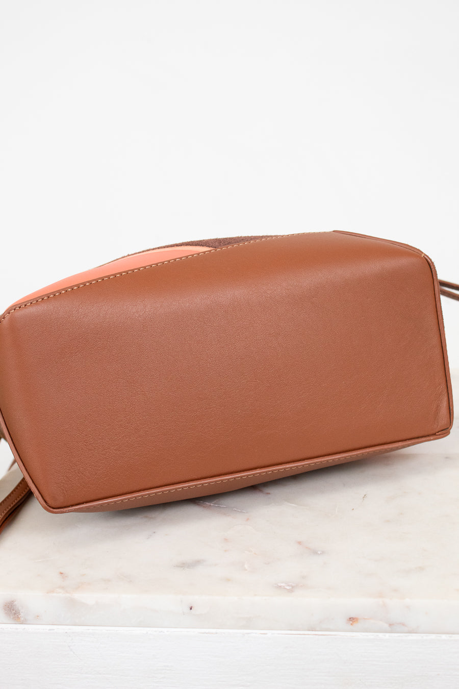 Brown leather handbag on a marble surface with a white background