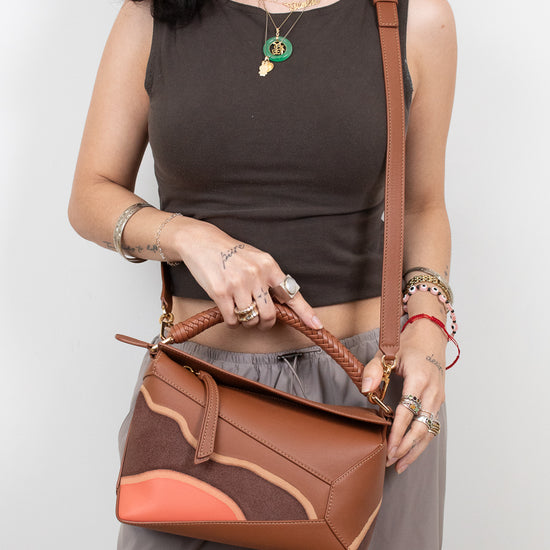 Woman holding a brown leather handbag against a plain background