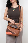 Woman holding a brown leather handbag against a plain background