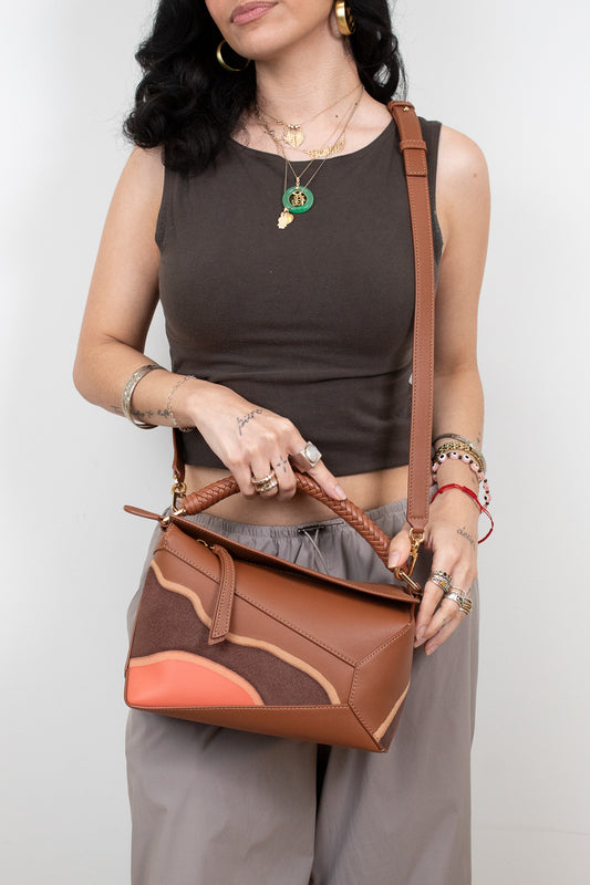 Woman holding a brown leather handbag against a plain background