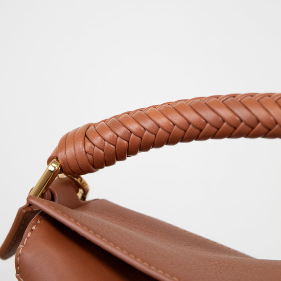 Close-up of a brown leather handbag with braided handle on a light gray background