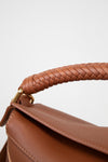 Close-up of a brown leather handbag with braided handle on a light gray background