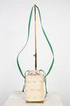 A cream woven bucket bag with embroidered daisy flowers, featuring a green shoulder strap and a gold-tone metal stand, set against a plain white background.