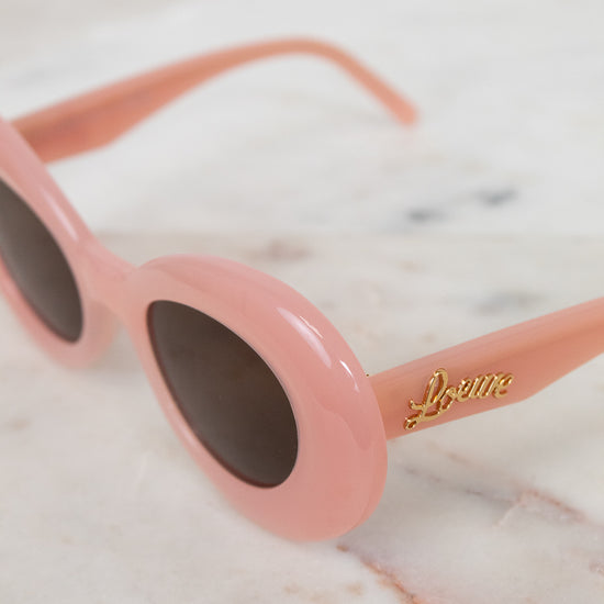 Pink sunglasses with a brand logo on a marble surface
