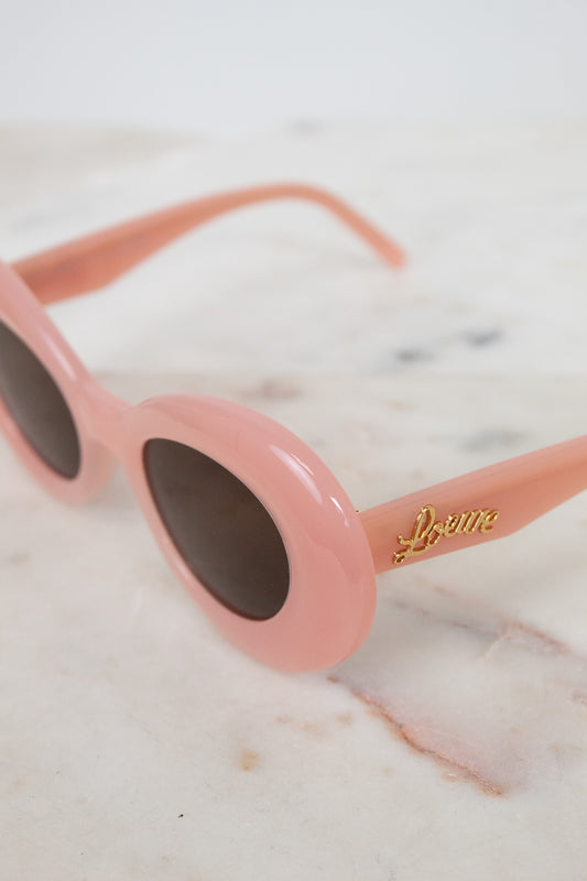 Pink sunglasses with a brand logo on a marble surface