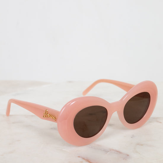 Pink sunglasses with gold logo on a white marble surface