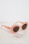 Pink sunglasses with gold logo on a white marble surface