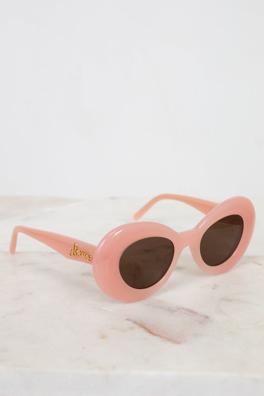Pink sunglasses with gold logo on a white marble surface