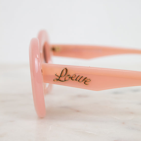 Pink sunglasses with 'Loewe' branding on a marble surface