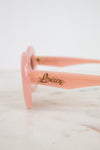 Pink sunglasses with 'Loewe' branding on a marble surface