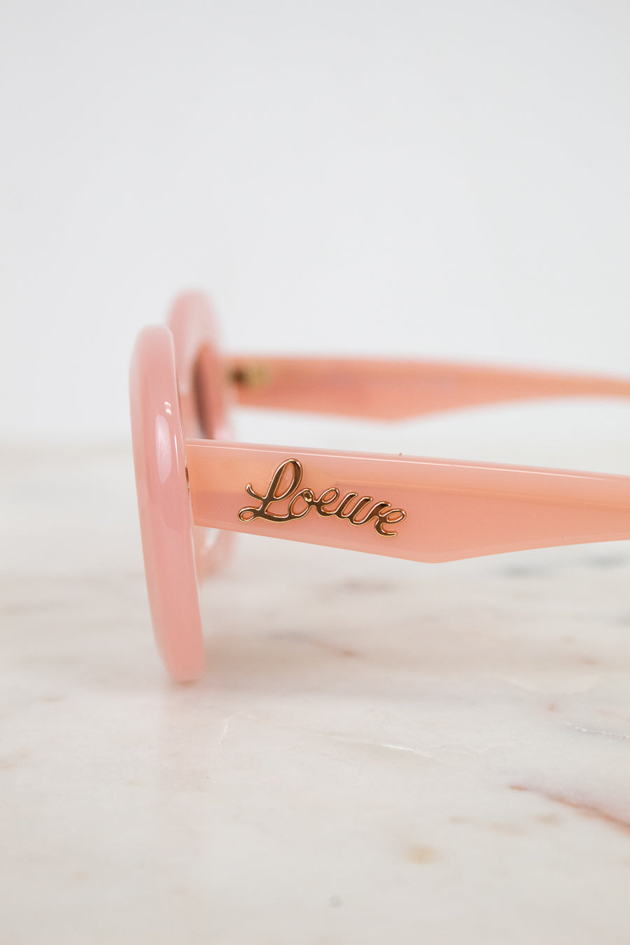 Pink sunglasses with 'Loewe' branding on a marble surface
