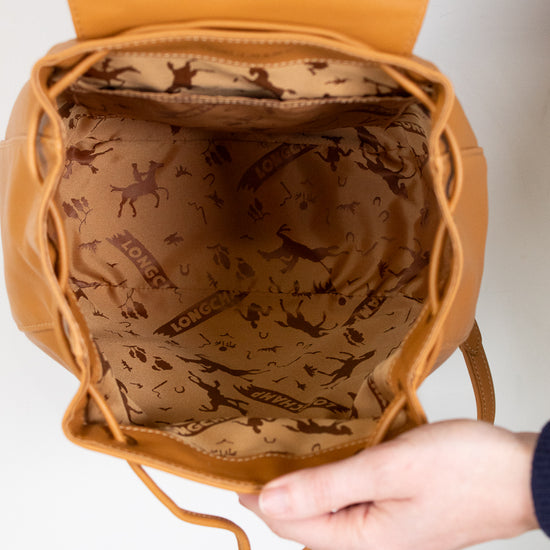 Brown leather bag with patterned interior held by a hand on a white background