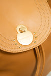 Close-up of a tan leather handbag with a gold clasp and decorative studs.