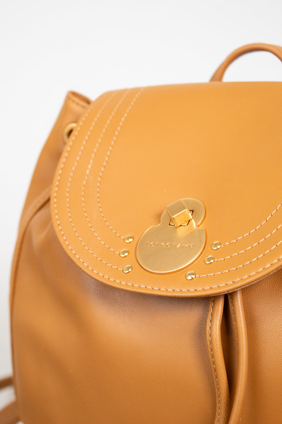 Tan leather backpack with a gold lock on a light gray background