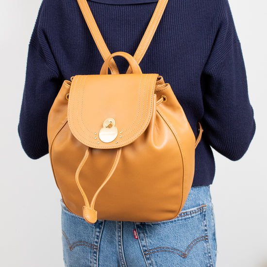 Person wearing a mustard yellow backpack with a plain background