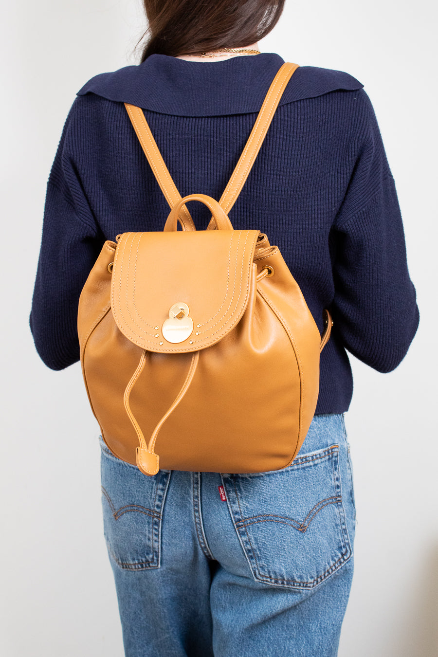 Person wearing a mustard yellow backpack with a plain background