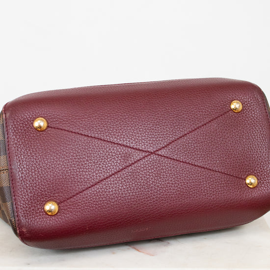 Maroon base of handbag with gold studs on a light gray background