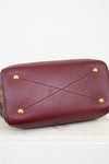 Maroon base of handbag with gold studs on a light gray background