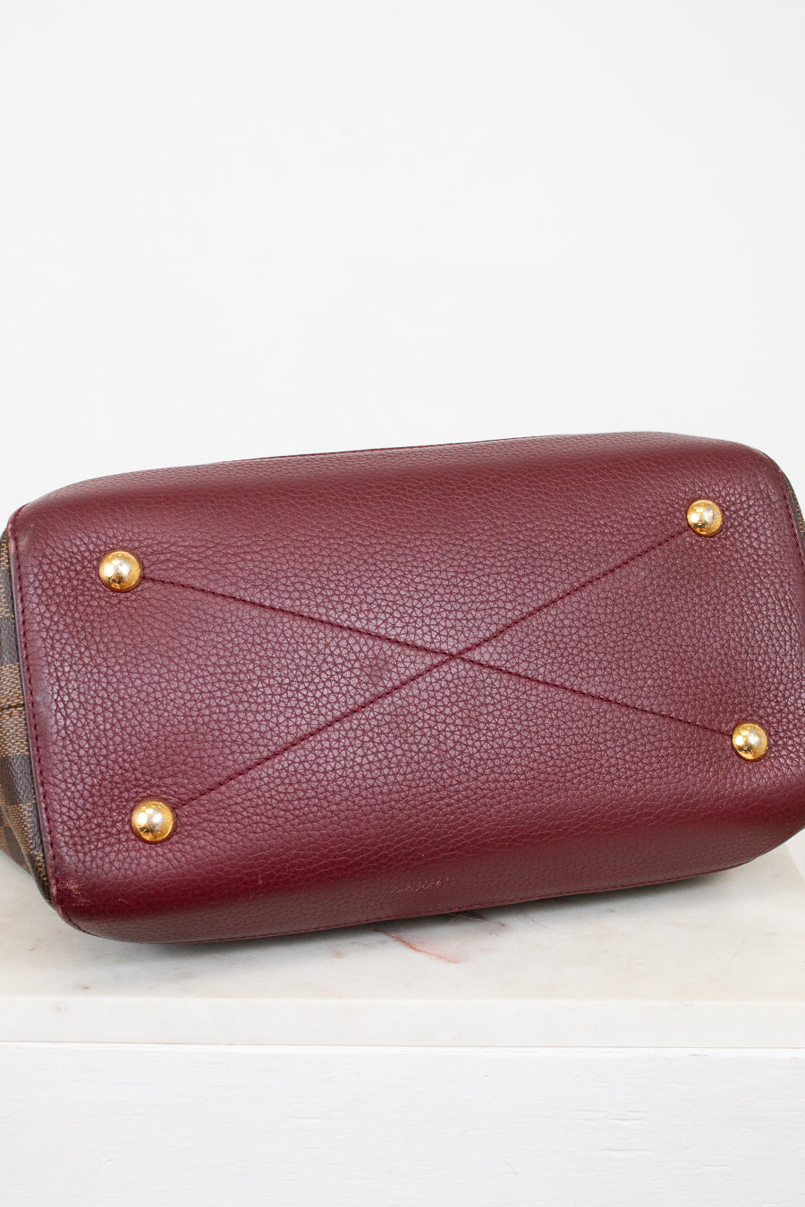 Maroon base of handbag with gold studs on a light gray background