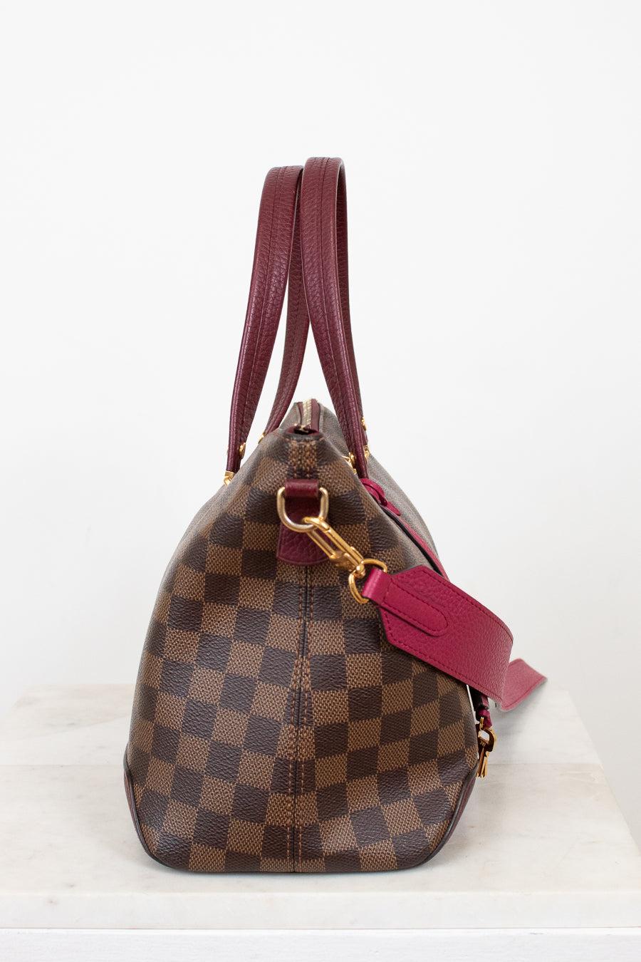 Designer handbag with brown checkered pattern and red strap on a white background