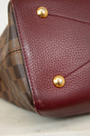 Close-up of a maroon leather handbag base with gold studs on a light background