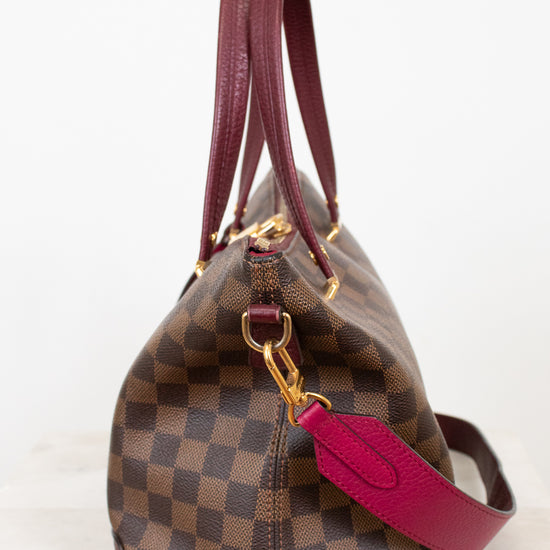 Designer handbag with brown checkered pattern and red handle on a white background