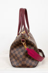 Designer handbag with brown checkered pattern and red handle on a white background
