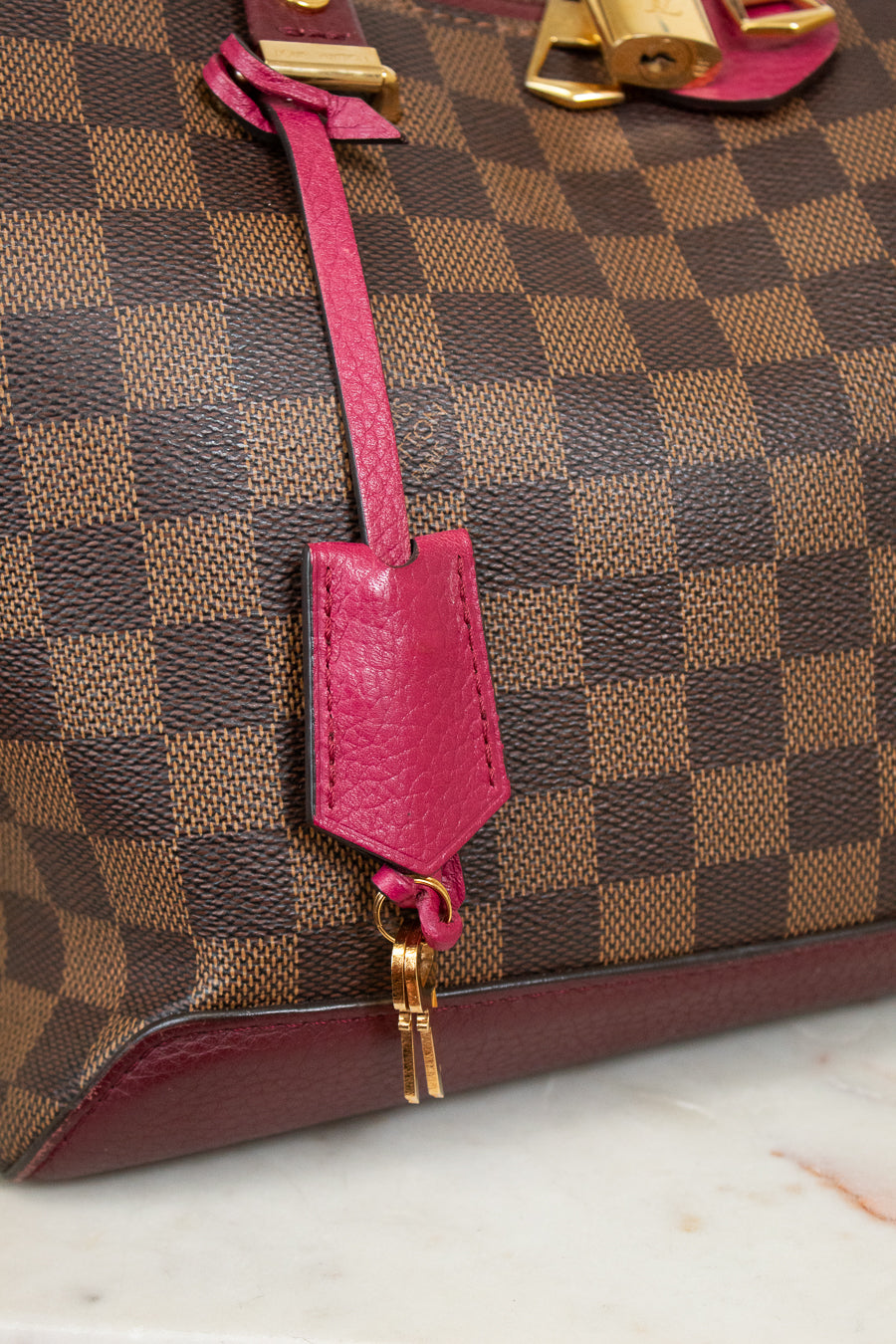 Designer handbag with a pink strap and gold hardware on a marble surface