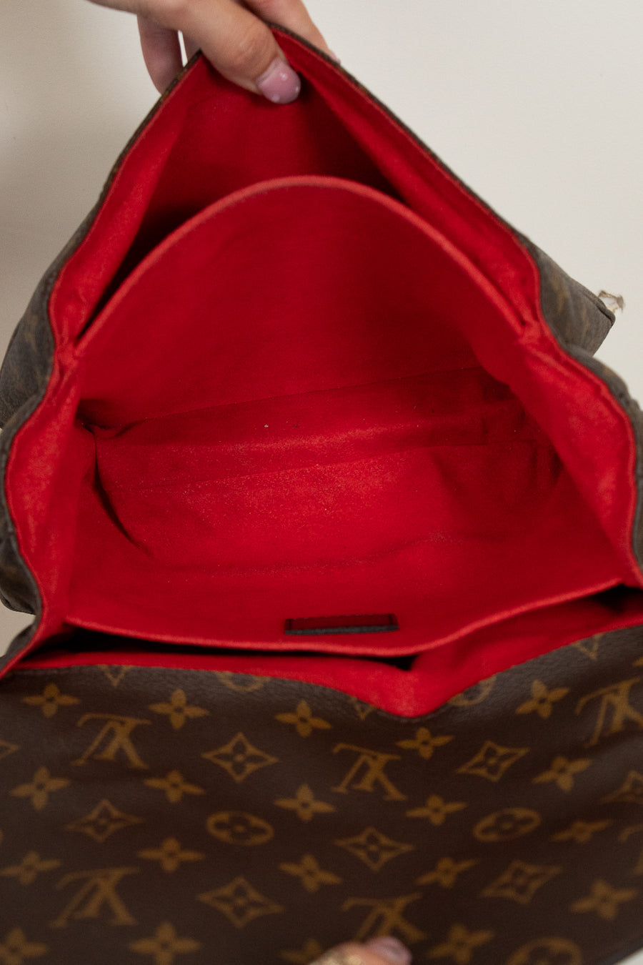 Brown leather bag with red interior, featuring a brand logo.