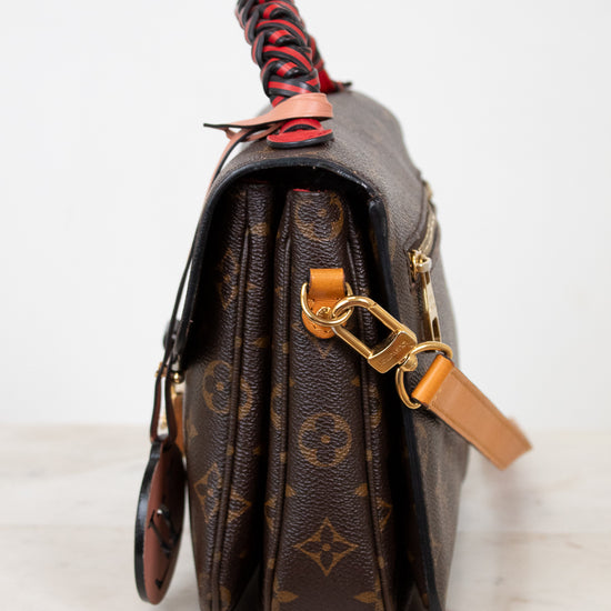 Brown monogrammed handbag with a red and black handle on a white background
