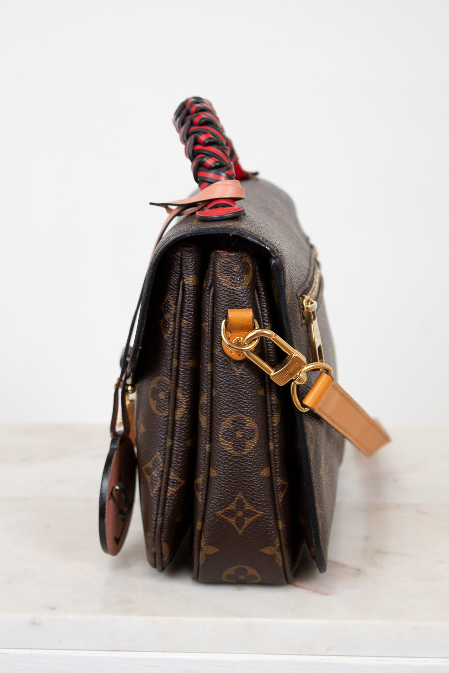 Brown monogrammed handbag with a red and black handle on a white background