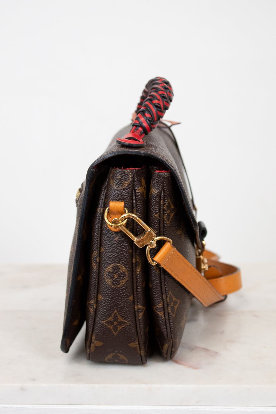 Brown monogrammed handbag with a red and black handle on a white background