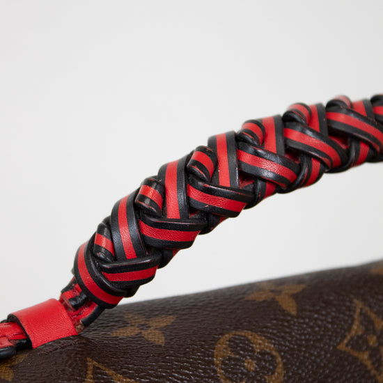 Close-up of a braided red and black leather strap on a Louis Vuitton monogram bag.
