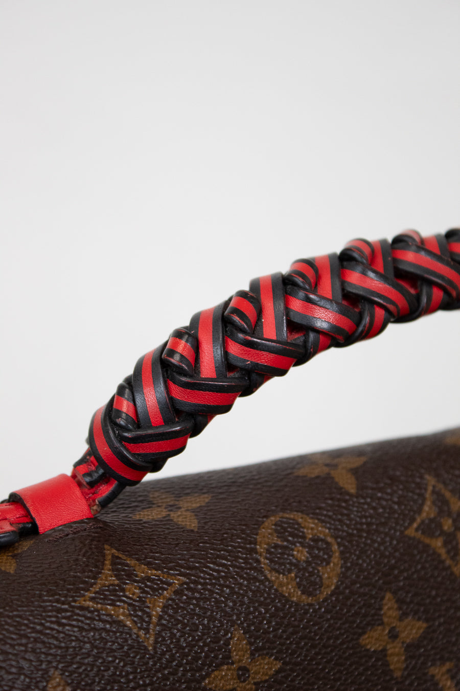 Close-up of a braided red and black leather strap on a Louis Vuitton monogram bag.