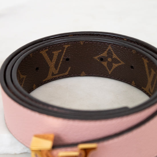 Pink belt with brown monogram pattern and gold buckle on a light background