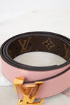 Pink belt with brown monogram pattern and gold buckle on a light background
