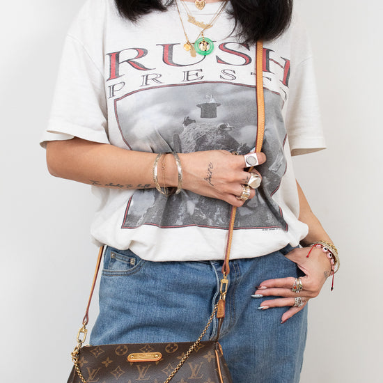 Person wearing a graphic t-shirt and jeans, holding a brown handbag against a white background
