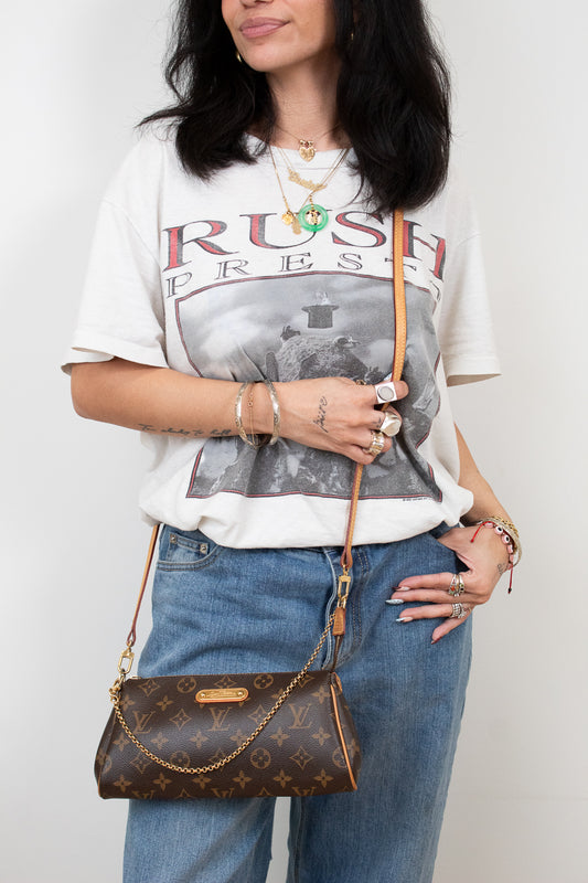 Person wearing a graphic t-shirt and jeans, holding a brown handbag against a white background