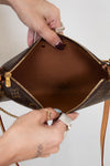 Close-up of a brown handbag with gold accents held by a person's hands.
