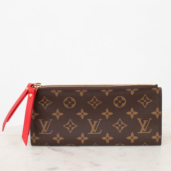Louis Vuitton wallet with monogram pattern and red zipper on a white marble surface