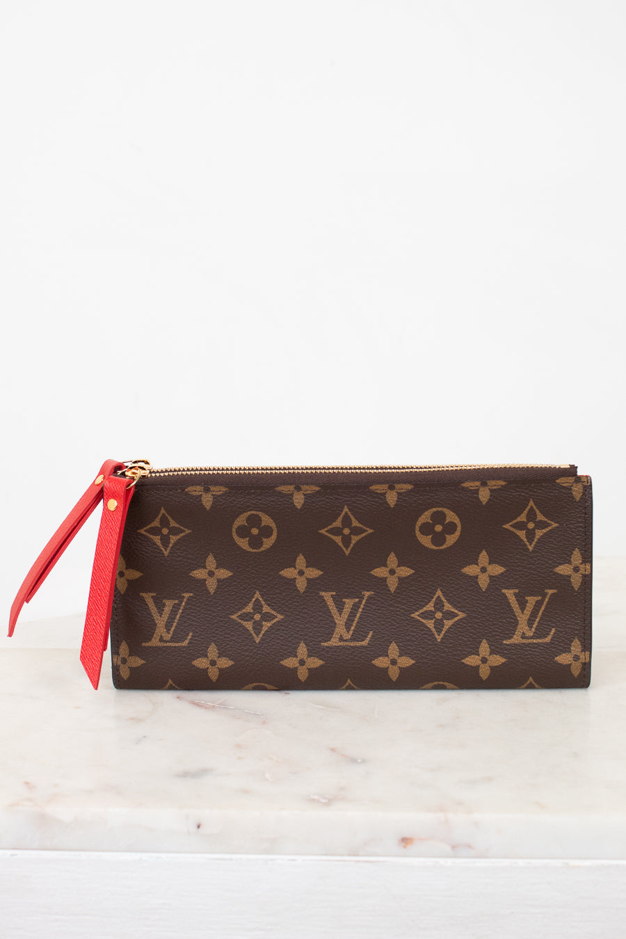 Louis Vuitton wallet with monogram pattern and red zipper on a white marble surface