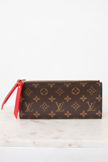 Louis Vuitton wallet with monogram pattern and red zipper on a white marble surface