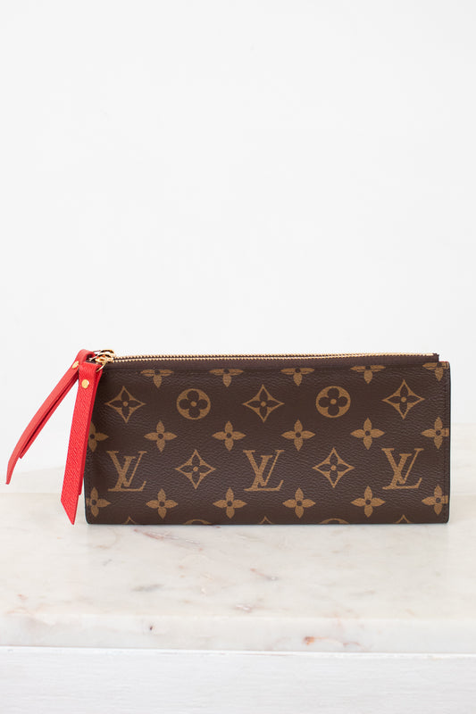 Louis Vuitton wallet with monogram pattern and red zipper on a white marble surface