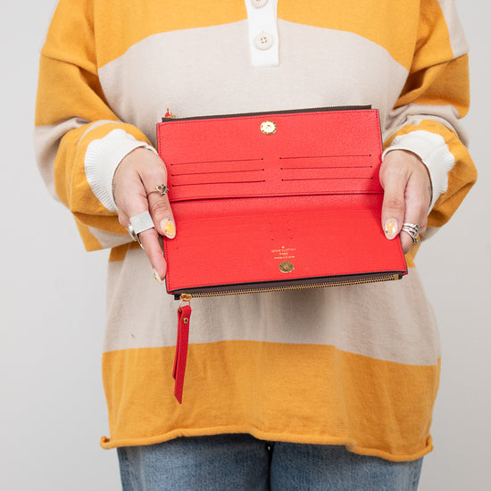 Person wearing a colorful striped shirt holding an open red wallet against a plain background