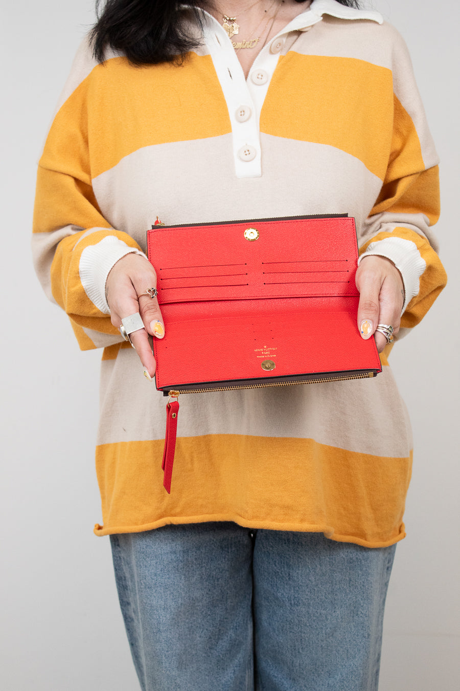 Person wearing a colorful striped shirt holding an open red wallet against a plain background