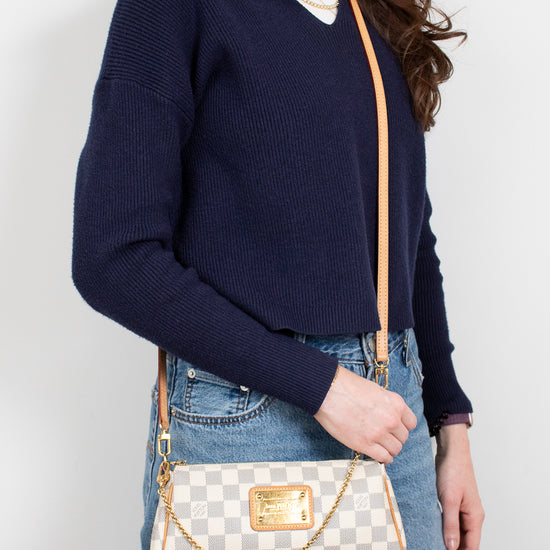 Person wearing a navy sweater and blue jeans, holding a checkered handbag against a plain background