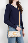 Person wearing a navy sweater and blue jeans, holding a checkered handbag against a plain background