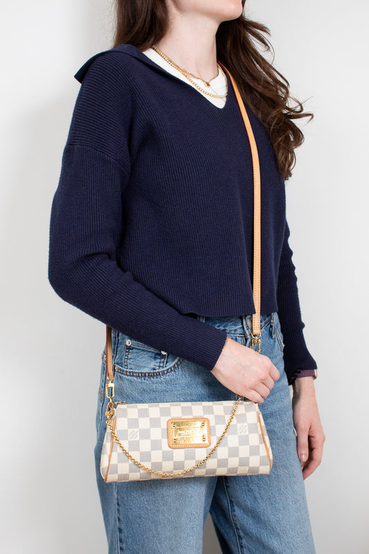 Person wearing a navy sweater and blue jeans, holding a checkered handbag against a plain background