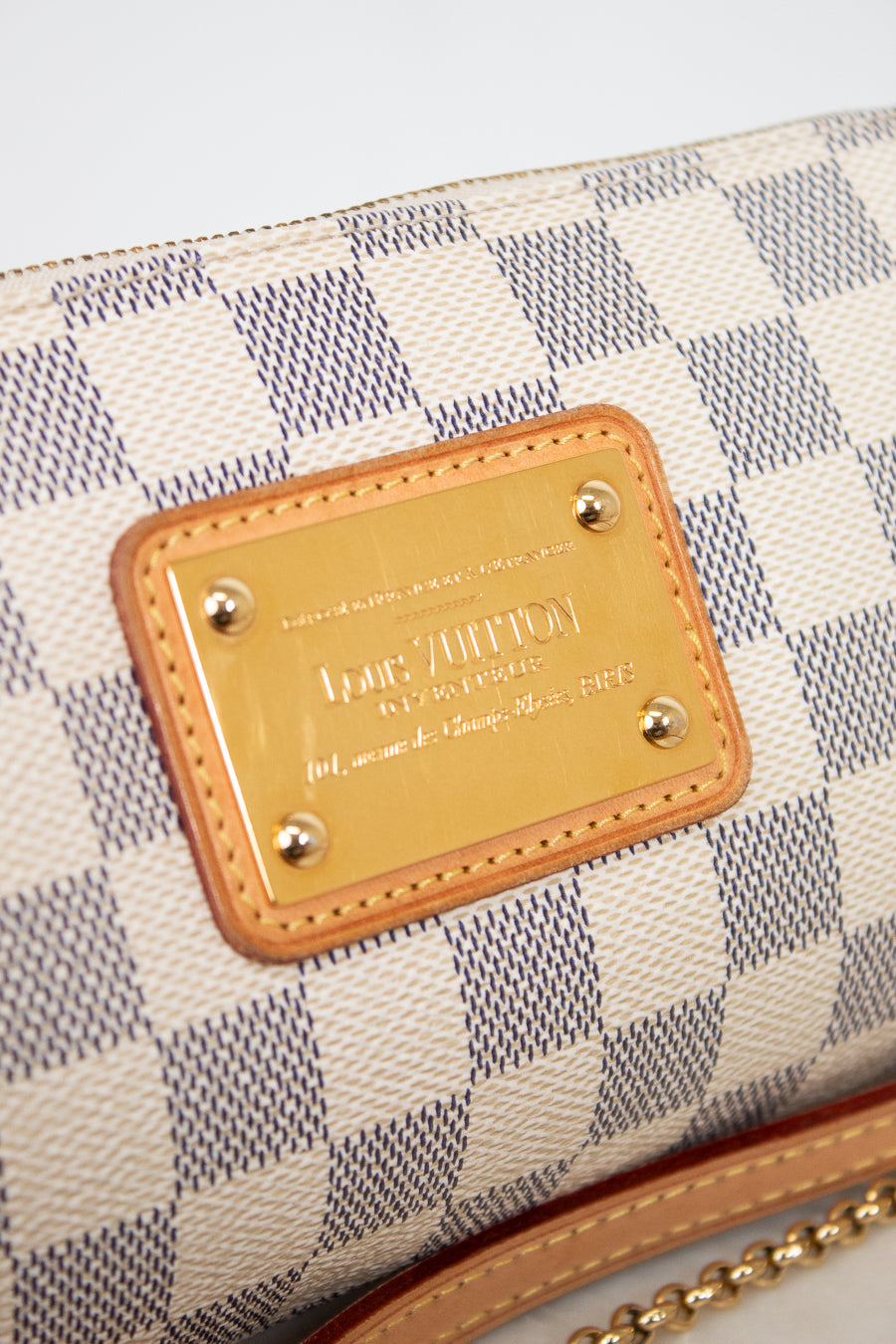 Louis Vuitton wallet with checkered pattern and gold plaque on a light gray background