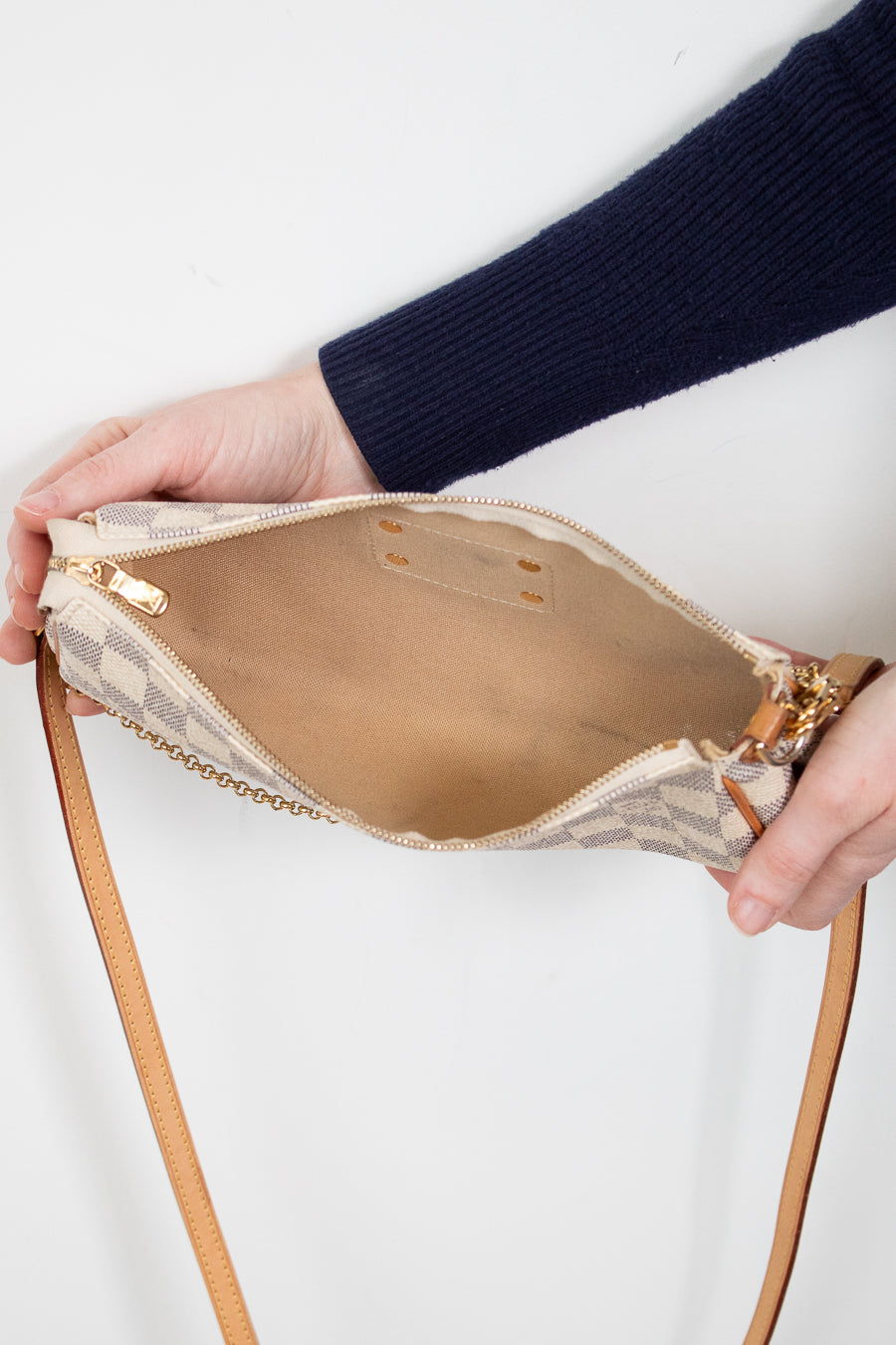 Person holding a beige handbag with a strap against a white background